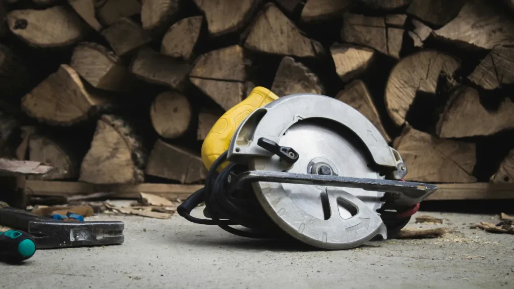Yellow corded circular saw resting on a concrete floor with a large stack of chopped firewood in the background.