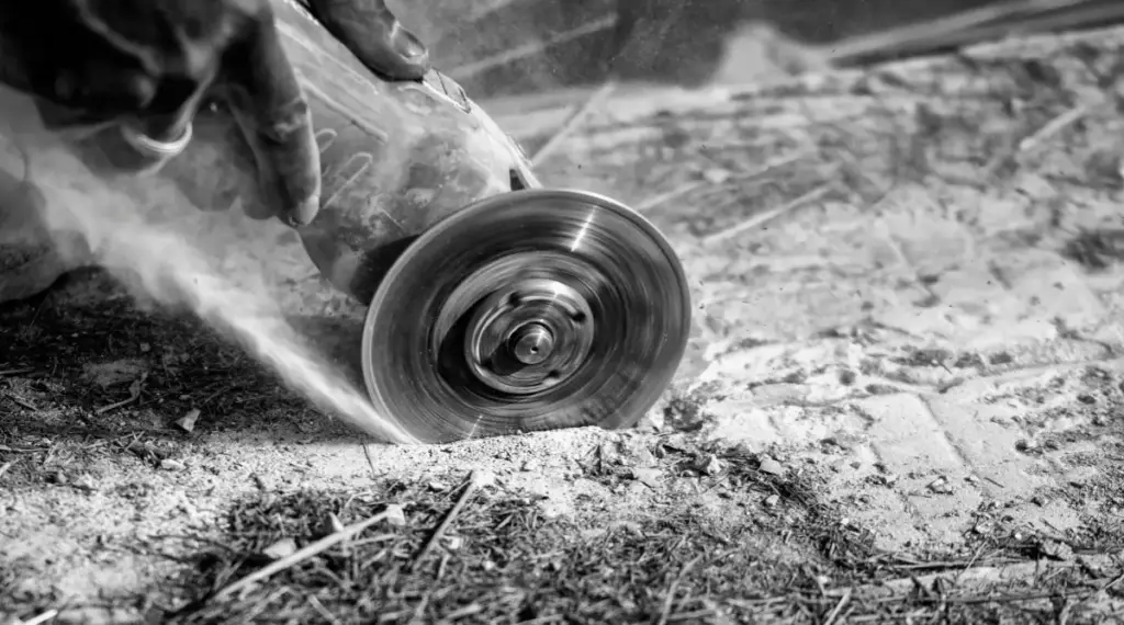 Close-up of a worker dry cutting concrete with a masonry blade, creating a thick plume of dust.