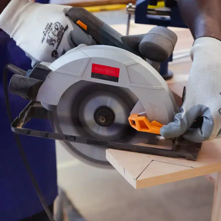 Close-up of a carpenter wearing safety gloves cutting a wooden board with a circular saw.
